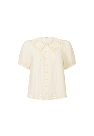 A cream-colored short-sleeve blouse with eyelet lace detailing on the collar and hem, featuring a button-down front and gathered bodice, shown against a plain white background.