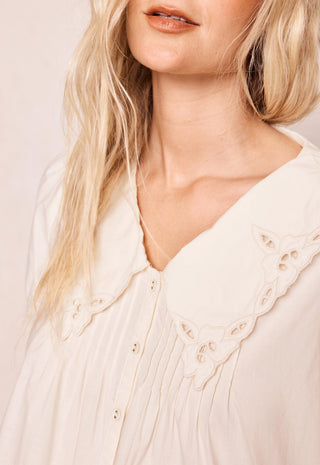 Close-up of a woman wearing a cream-colored blouse with a large scalloped eyelet collar and button front.