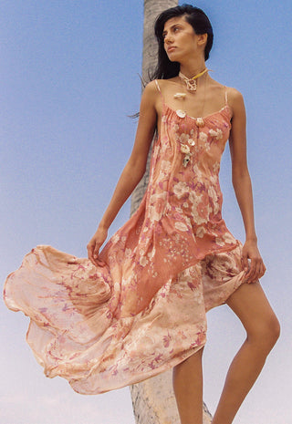 A woman wearing a flowing floral slip dress in soft pink and peach tones
