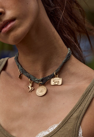 a-close-up-of-a-woman-wearing-a-dark-olive-green-braided-leather-choker-necklace-with-gold-toned-animal-and-circular-pendant-charms