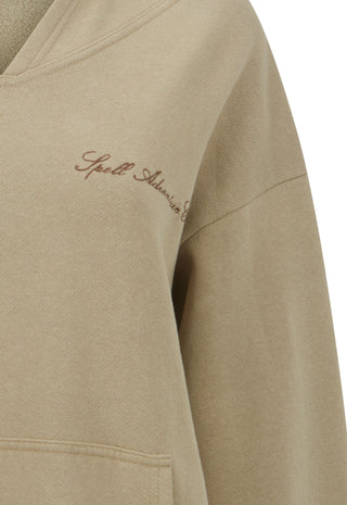 Close-up of a beige sweatshirt sleeve with a small brown embroidered script logo on the upper chest, photographed against a white background.
