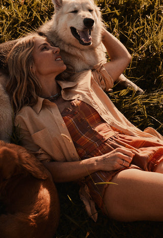  wearing a rust-orange plaid romper and a light beige button-up shirt. The scene is lit by warm golden sunlight.