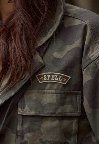 close-up-of-a-person-wearing-a-camouflage-utility-jacket-showing-the-chest-pocket-with-a-sewn-spell-patch-on-the-left-chest