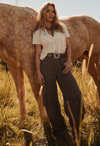 A woman stands in a field of dry grass next to a horse