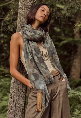 a-woman-in-a-forest-setting-wearing-a-camouflage-print-scarf-draped-over-her-shoulders-paired-with-a-beige-tank-top-and-brown-cargo-pants